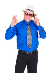Happy and successful businessman in blue shirt, tie, sunglasses and white hat. Speaking by cell mobile phone, holding notebook under his arm and show gesture Ok. Isolated white background