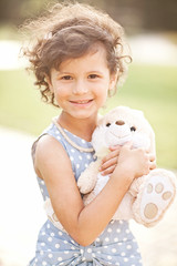 Little cute curly girl hands embraces an white soft rabbit toy.