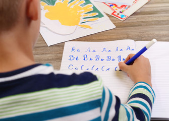 School Boy Writing on Paper writing the alphabet with Pencil . Kid, homework, education concept