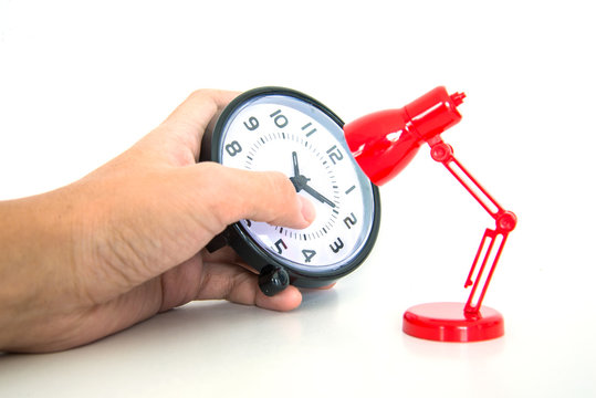 Hand holding alarm clock with red desk lamp