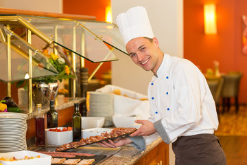 Cook or chef filling buffet at restaurant with cold meat