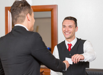 receptionist at hotel reception handing key card to guest