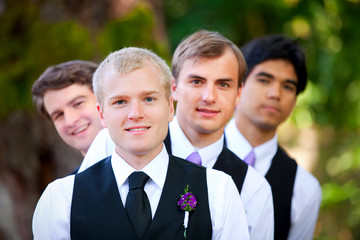 Groomsmen peeking from behind groom, outdoor