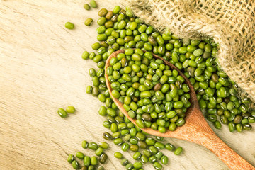 close up green mung beans in wooden spoon on wood plate
