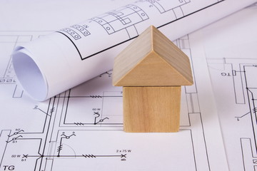 House of wooden blocks and rolls of diagrams on construction drawing of house