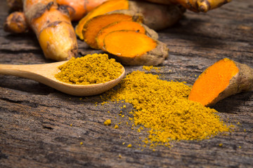 turmeric powder in spoon and roots on wooden plate - Powered by Adobe