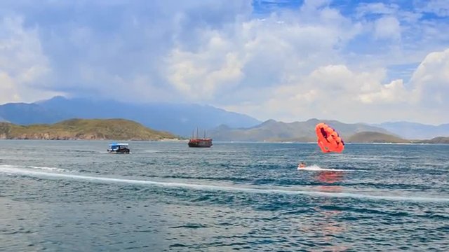 parasailer touches water takes off over azure sea against hills