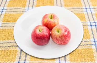 Three red apples on a white dish