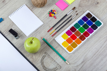 Naklejka premium Paper, pencils, brush, green apple on wooden table