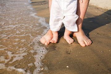father and baby feet walking on sand beach