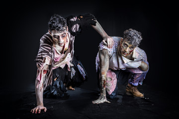 Two male zombies crawling on their knees, on black smoky