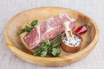 A piece of fresh marbled beef, chili pepper, parsley, onion, garlic, ribs lie on a wooden tray