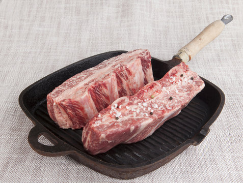 Close-up of two pieces of fresh marbled beef with sea salt and black pepper, on a cast-iron grill pan