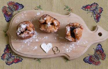 Three donuts with cherry on the cutting board with sugar heart on tablecloth with butterflies. Aerial view.