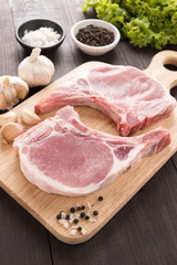 Raw pork chop steak and garlic, pepper on wooden background