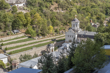 Fototapeta na wymiar Bakhchisaray , Crimea , Russia . Holy - Assumption Orthodox cave Monastery .The lower tier of the monastery. One of the new church , a small cemetery , outbuildings , land for vegetable gardens .