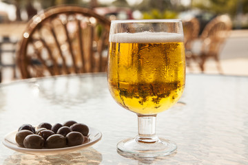 Misted glass of beer with olives on a glass table