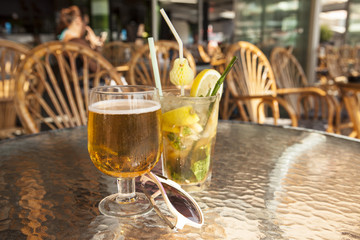 Misted glass of beer and mojito  with olives on a glass table