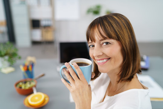 glückliche geschäftsfrau mit einer tasse kaffee am schreibtisch