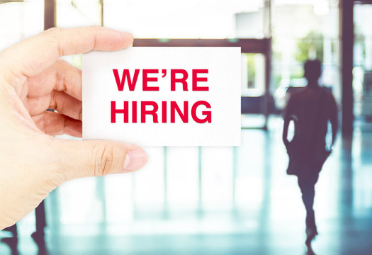 Hand holding Business card with We 're hiring word at blur corri