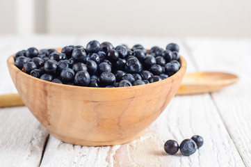 Wooden bowl with forest blueberry on white wooden background
