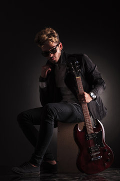 young guitarist sitting and holding his jacket by it's collar