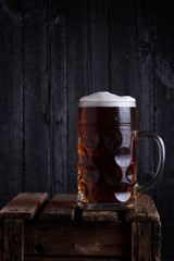 Huge beer mug on vintage wooden crate with dark wooden background still life