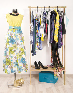 Dressing closet with colorful clothes arranged on hangers and a summer outfit on a mannequin.Wardrobe with clothes and accessories. Tailor's dummy wearing a long floral skirt with a yellow top.