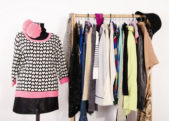 Wardrobe with winter clothes arranged on hangers and an outfit on mannequin.Dressing closet with autumn clothes and accessories. Tailor's dummy wearing a cute  sweater, black skirt and pink earmuffs.