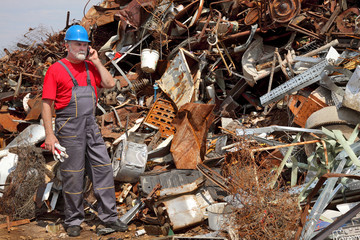Recycling industry, heap of old metal and worker speaking by phone