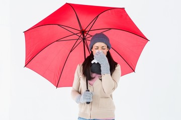 Sick brunette blowing her nose while holding an umbrella