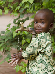 Young African school boy holding hands under a tap. Water scarcity problems concern the inadequate...