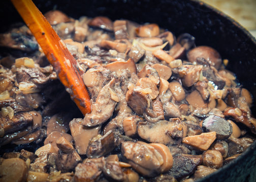 Wild mushrooms and onions fried in a cooking pan with a wooden paddle
