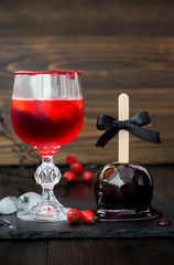 Spooky bloody cocktail and black poison caramel apple. Traditional dessert and drink recipe for Halloween party. Selective focus