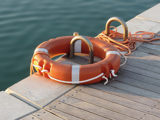 Fototapeta premium Orange life buoy on wooden pier in the harbor in Marina di Pisa, Tuscany, Italy