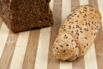 Rye bread and roll mixed from many different healthy ingredients like pieces of soy, rye and wheat flour, sunflower seeds and barley. Studio shot. Photographed on interesting wooden table.
