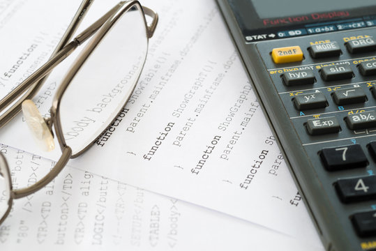 Closeup glass and calculator place on programming code papers