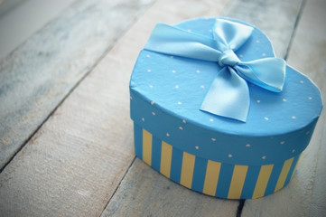 Heart shaped gift box decorated with a blue ribbon, all on a white wooden table. Empty copy space for editor's text.