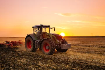 Crédence de cuisine en verre imprimé Tracteur Tracteur sur le champ d& 39 orge au coucher du soleil.