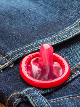 Closeup red condom on jeans pocket.