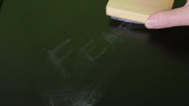 Hand holding eraser wiping the word Fear off a blackboard.