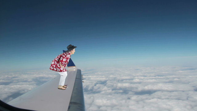 Woman dressed in tacky Hawaiian shirt and sandals riding on the outside of an airplane on the wing looking and waving at passengers.