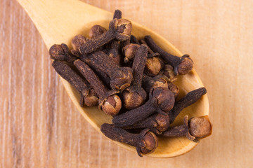 Heap of cloves with wooden spoon on table, seasoning for cooking