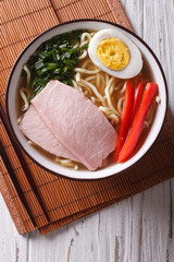 Ramen noodles in broth with pork in a bowl close up. vertical top view
