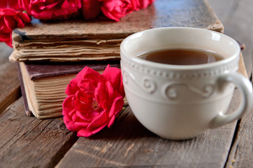 Old books with beautiful flowers and cup of tea on wooden table close up