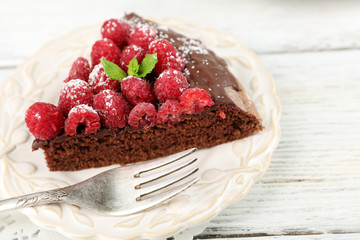 Piece of cake with chocolate Glaze and raspberries on color wooden background