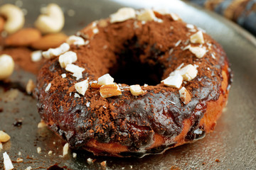 Delicious doughnut with chocolate icing and nuts on plate close up