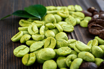 Green and brown coffee beans with leaves on wooden table close up