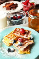 Sweet homemade waffles with forest berries on plate, on light background