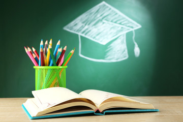 Metal cap of crayons with open book and bachelor hat drawing on blackboard background